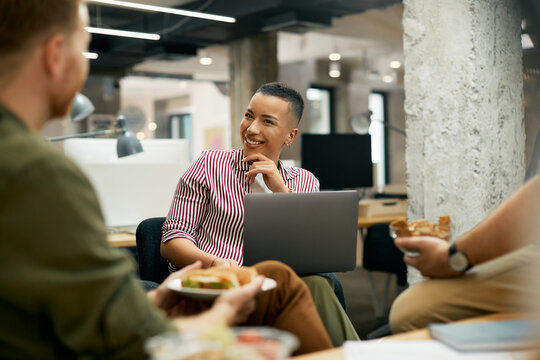 Happy African American businesswoman using laptop and communicating with coworkers on a break in the office.