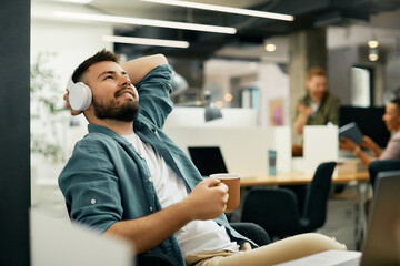 Smiling freelancer with headphones daydreaming during coffee break in the office.