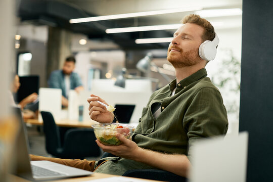 Relaxed businessman enjoying in music over headphones on lunch break in the office.