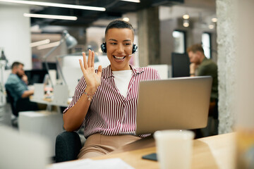 Happy African American businesswoman greeting someone during video call while working in the office.
