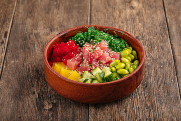 Hawaiian tuna poke bowl with vegetables on wooden background