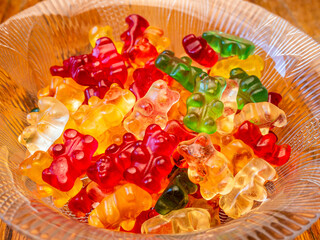 Glass bowl with colorful gummy bears, on a wooden background - selective focus