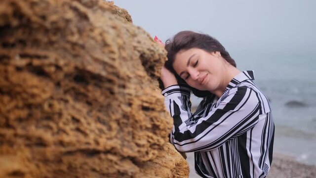 Beautiful young woman stands at the rock resting. Gorgeous style brunette female in long dress standing on a cliff near sea, sand tropical on rock. Lonely melancholy waiting freedom