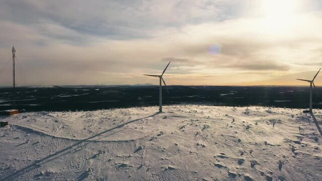 Aerial view of wind turbines rotating on top of a snowy fell, in Lapland - pull back, drone shot