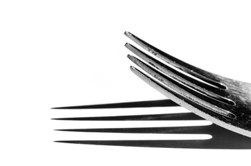 Closeup of a fork horizontally on a white surface, with a harsh shadow
