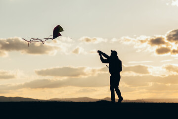 Silhouette of hipster guy flying a kite at sunset. 