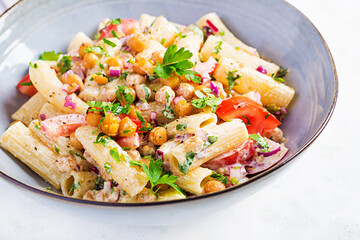 Vegetarian vegetable pasta. Pasta rigatoni with tomato, red onion, parsley and fried chickpeas with nut sauce. Vegan food.