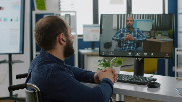 Invalid paralized handicapped freelancer talking on videocall with remote coworker with disabilities sitting immobilized in wheelchair discussing online from start-up office during virtual meeting