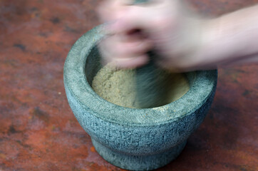 Blurry motion. A hand grinds with a pestle spices and herbs in a