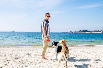 young man playing with dog and ball on the beach