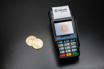 Payment terminal ready to accept bitcoins for payment. There are gold bitcoin coins on the black table nearby