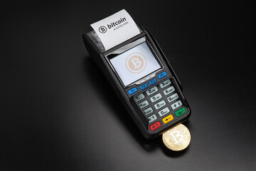 Payment terminal ready to accept bitcoins for payment on the black background. Bitcoin gold coin sticks out of the POS terminal