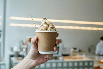 Hand holding a coffee soft serve ice cream. A paper cup of ice cream with coffee flavour, ice cream made of arabica coffee bean at coffee cafe.