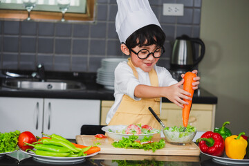 Asian Boy son cooking salad food holdind wooden spoon with vegetable holding tomatoes and carrots, bell peppers on plate for happy family cook food enjoyment lifestyle kitchen in home
