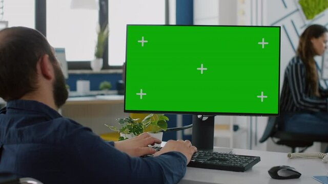 Paralized invalid businessman sitting in wheelchair with green screen chroma key display, typing on computer while team working on background. Multiethnic coworkers planning project of strat up
