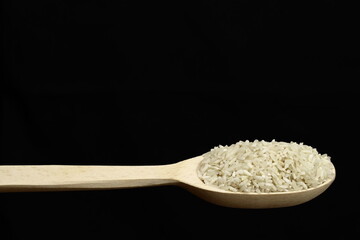 Raw rice grits in a wooden spoon on a black background