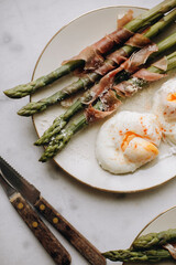 asparagus with boiled poached eggs. boiled green asparagus garnished with prosciutto or ham. healthy and tasty breakfast with asparagus. snack with asparagus top view.