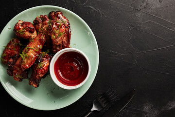 chicken wings with ketchup on a light plate on a black textured background top view