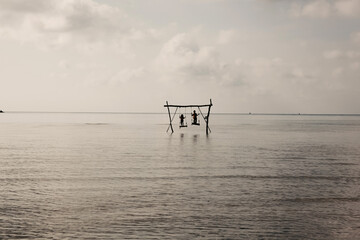 Fototapeta na wymiar Black and white photo of Two kids playing and standing on wooden swing over calm sea water at Karimun Jawa