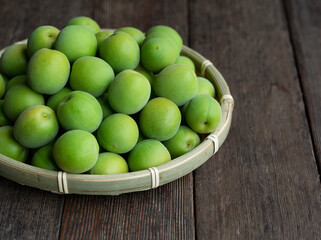 Plum fruit in a bamboo colander placed in the wooden background.