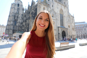 Beautiful smiling tourist girl taking self portrait with smartphone in Vienna with Saint Stephen's cathedral on the background in Austria, Europe