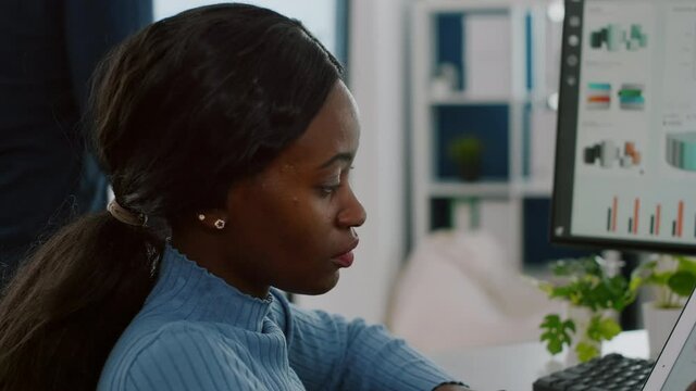 African invalid manager woman paralyzed in wheelchair using computer and tablet in same time working for financial project in business startup office. Focuse black employee using modern technology