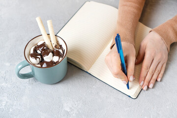 Girl writes in a diary or notepad. Tasty cup of cocoa nearby.