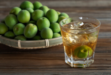Plum wine and unripe plums on a wooden background..