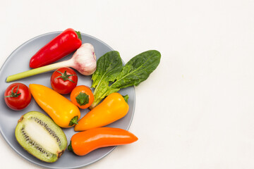 Half kiwi, garlic, peppers of different colors and tomatoes, spinach leaves on gray plate