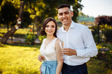Young couple with glasses in their hands at the wedding celebration. Portrait of a happy man and woman against the backdrop of a beautiful garden. Celebration, wedding concept, new family.