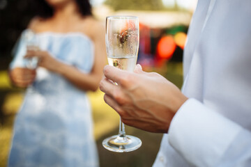 A man with a glass of champagne in his hands against the background of a company of celebrating people. Wedding, birthday, anniversary. Group of people enjoying champagne at wedding party.