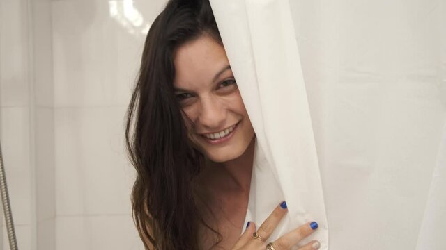 woman peeking from behind shower curtains in the bathroom. cute naked sexy girl looking from the shower and smiling at the camera. Lady in the shower. shy and teasing gestures flirting with the camera