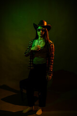 Obraz na płótnie Canvas A girl in a plaid shirt with a cowboy hat illuminated by multicolored light