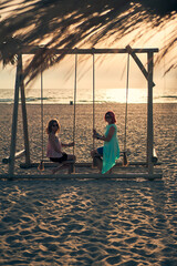 Two young attractive women resting on seesaw on the beach at sunset.