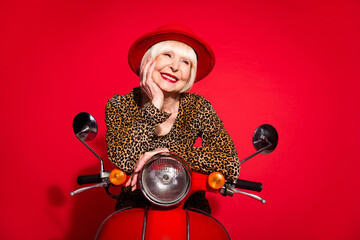 Photo of cheerful aged woman happy positive smile drive bike trip hand touch cheek isolated over red color background