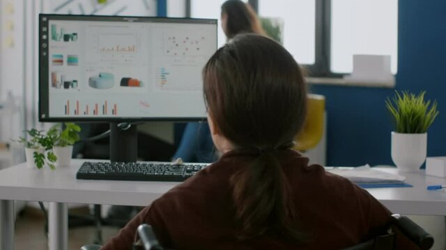 Independece invalid woman manager with disability comming with wheelchair at workplace starting to work at financial project typing at pc with data prosessing on display, for project regarding economy