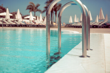 Hotel swimming pool side with blue water, close-up shot, with sunbeds on background