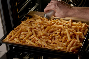 Crop person adding salt to crinkle fries