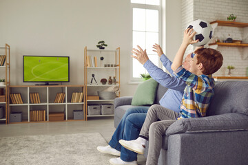 Senior grandfather and preteen grandson fan watching soccer match on tv cheering for football team...