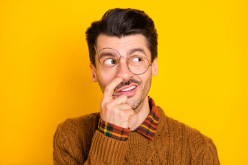 Photo of foolish nerd guy finger nose look empty space wear glasses brown sweater isolated yellow...