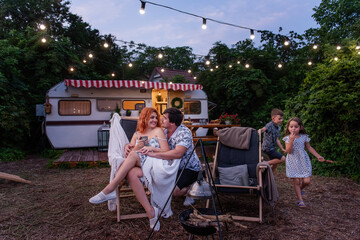 Middle-aged parents sit on wooden sun loungers by the motor house, their daughter and son are...