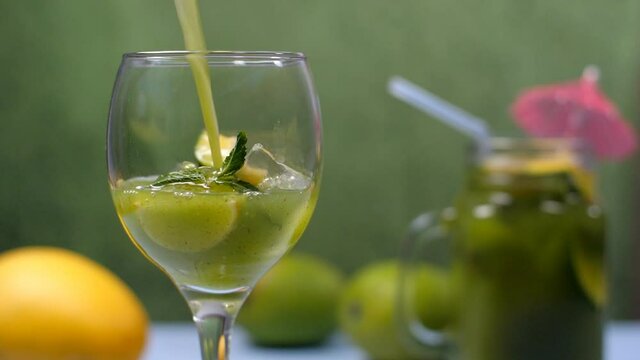 Pouring of Kairi Panna in clear glass with mint leaves and lemon slice - Aam Panna  Summer drink in India. Closeup shot of a glass jar with fresh juice decorated with a cocktail umbrella and mangoe...