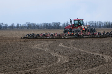 red tractor in a field rear view, tractor with a plow on an agricultural field. big red tractor working in the field, harvesting, business, agriculture. soil preparation, spring season. Ukraine