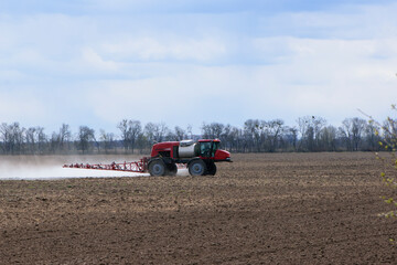 Obraz premium Red tractor with irrigation system watering a field on a cloudy day. agricultural machinery, work in the field. seasonal work. tractor fertilizes the ground. rides in the field, small tractor