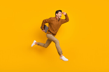 Full size profile photo of impressed nice brunet man hold laptop run wear sweater isolated on yellow background