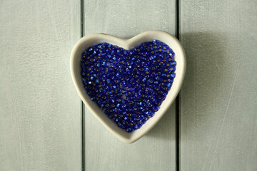 Blue beads in the Heart shaped plate on a wooden background.