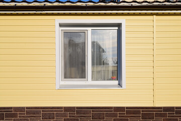 The wall of a private house with a window covered with yellow siding