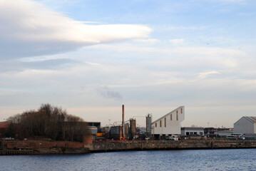 Fototapeta na wymiar Chimney & Industrial Buildings seen across River against Cloudy Sky 