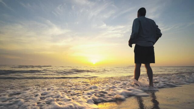 Man with extended arms spinning on the sea shore at sunrise, sunset while on tropical vacation. Success, vacation and happiness concept