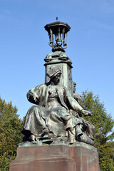 Fototapeta na wymiar Sculpted Female Figure and Ornate Victorian Lamp against Blue Sky 